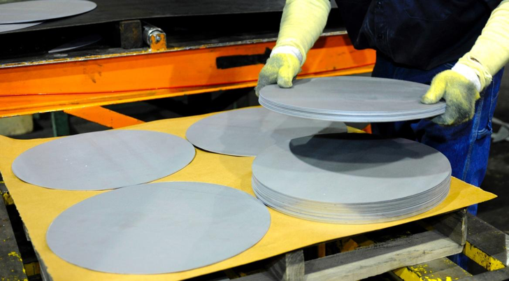 Four stacks of circular steel blanks with someone adding an additional blank to a stack