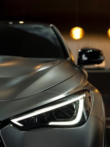 Close-up of a sliver luxury car, illuminated in a dark garage. The steel curves of the car catch the soft, warm light.