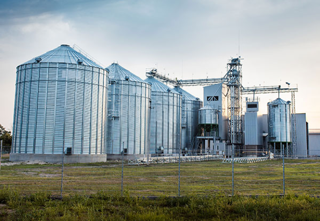 A wide angle of four large galvanized agricultural grain bins on an overcast day.