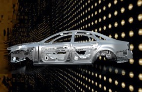 A computer graphic of the skeletal steel frame of a four-door sedan floating in front of a backdrop of a 3-D wall with uniform rows of small round lights.