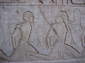 A stone carving in the Egyptian style depicting the profile of two bound, bearded men on their knees with a rope around their necks and arms behind their backs