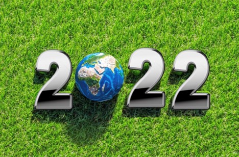 A photograph of a sunny, green lawn with the shadows of a 3D graphic of the text “2022” the zero is a globe.