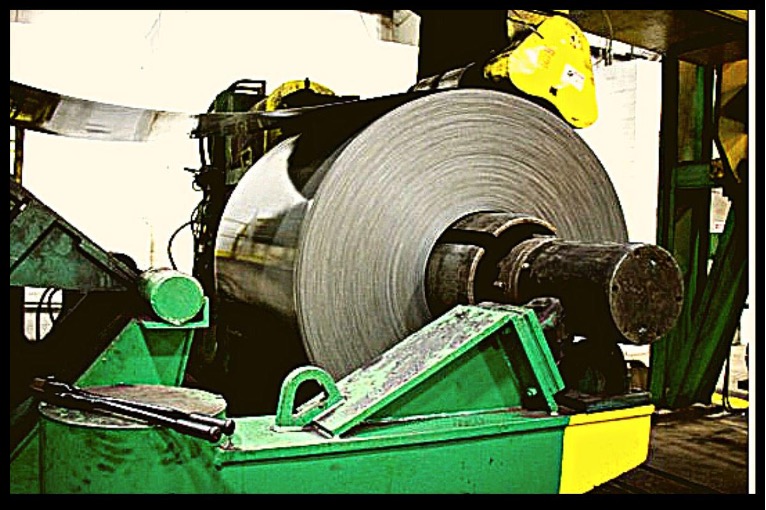 A huge roll of a stainless-steel sheet loaded onto the gigantic uncoiler machine at the at the beginning stages of the form rolling process.