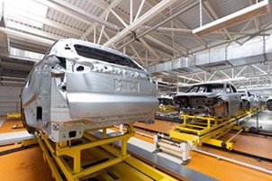 This depicts the interior of a car manufacturing plant, with car bodies at various stages of assembly arranged on a production line. The scene captures an industrial setting, with numerous machines and equipment involved in car-making.